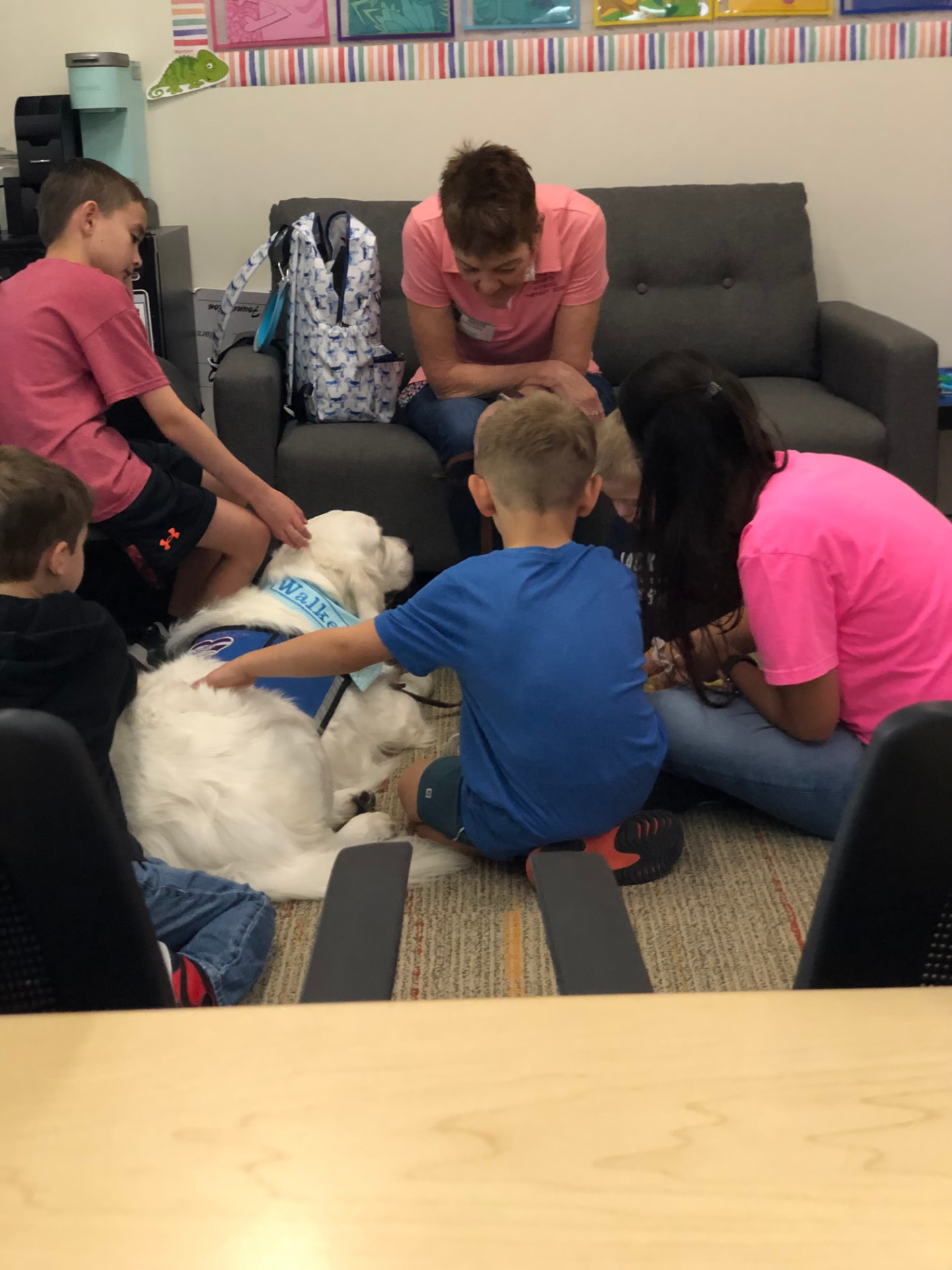 Children and adults gathered around Walker, a white therapy dog, during a school visit