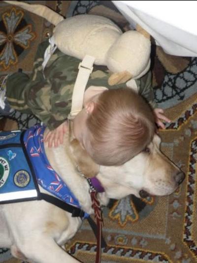 A young child in camouflage hugging therapy dog Chase