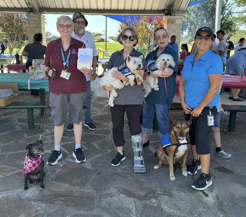 Therapy dog volunteers posing together with their dogs at an outdoor dog fair