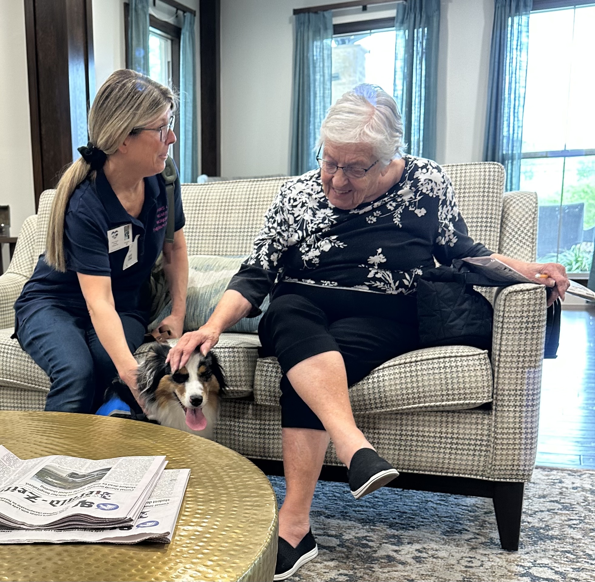 Boo the Australian shepherd therapy dog greeting a smiling resident in an assisted living living room